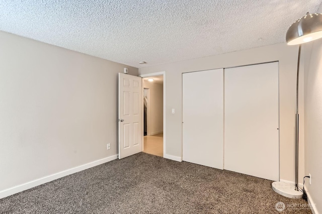 unfurnished bedroom featuring a textured ceiling, a closet, dark carpet, and baseboards