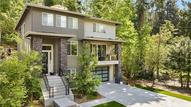 contemporary home with a garage, concrete driveway, a balcony, and stucco siding