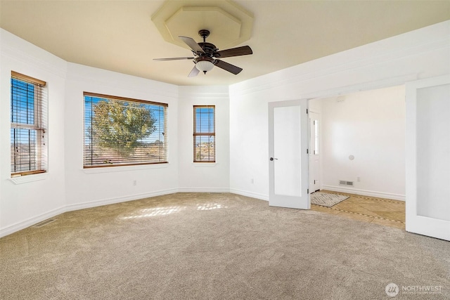 carpeted empty room with visible vents, ceiling fan, and baseboards