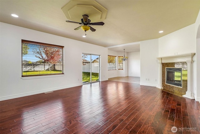 unfurnished living room featuring ceiling fan with notable chandelier, a fireplace, wood finished floors, and baseboards