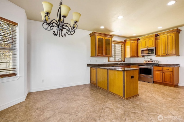 kitchen featuring baseboards, glass insert cabinets, brown cabinets, a peninsula, and stainless steel appliances