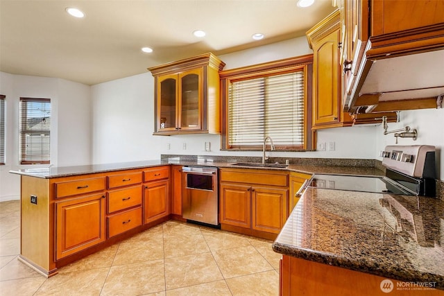 kitchen with brown cabinetry, glass insert cabinets, appliances with stainless steel finishes, a peninsula, and a sink