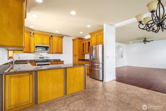 kitchen featuring ceiling fan, stainless steel appliances, a peninsula, a sink, and dark stone countertops