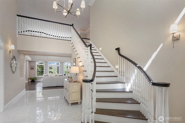 stairs featuring marble finish floor, a high ceiling, baseboards, and a notable chandelier