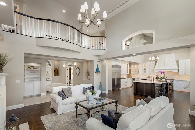 living area featuring baseboards, dark wood finished floors, a towering ceiling, a notable chandelier, and recessed lighting