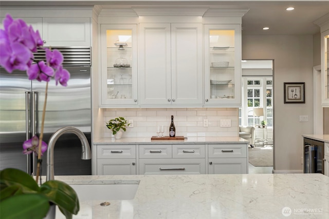 kitchen featuring tasteful backsplash, white cabinets, glass insert cabinets, stainless steel built in fridge, and a sink