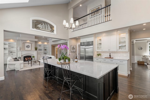 kitchen featuring open floor plan, stainless steel built in fridge, white cabinets, a warm lit fireplace, and a kitchen breakfast bar