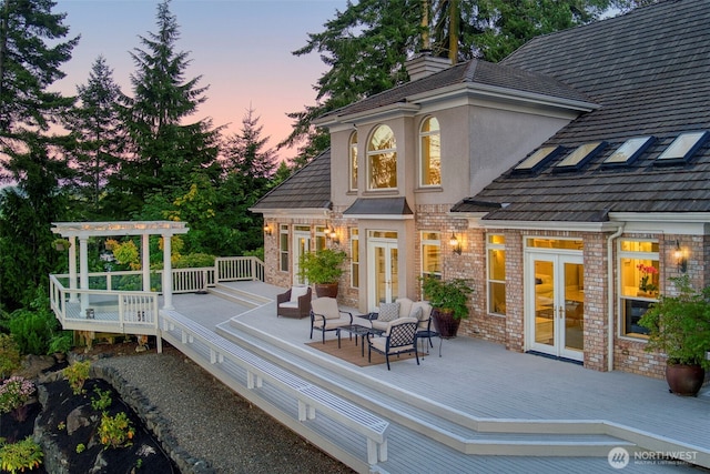 back of property with a deck, brick siding, french doors, a pergola, and stucco siding