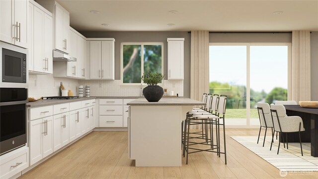 kitchen with light wood-style floors, a breakfast bar area, a center island, under cabinet range hood, and stainless steel gas cooktop