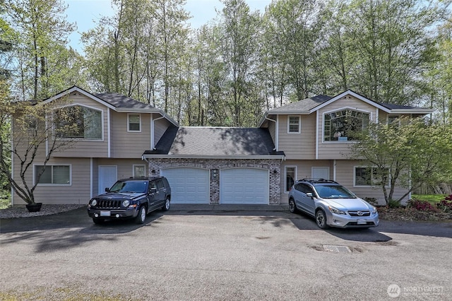 split level home featuring stone siding, a garage, driveway, and roof with shingles