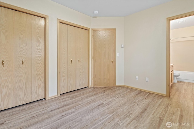 unfurnished bedroom featuring visible vents, multiple closets, wood finished floors, connected bathroom, and baseboards