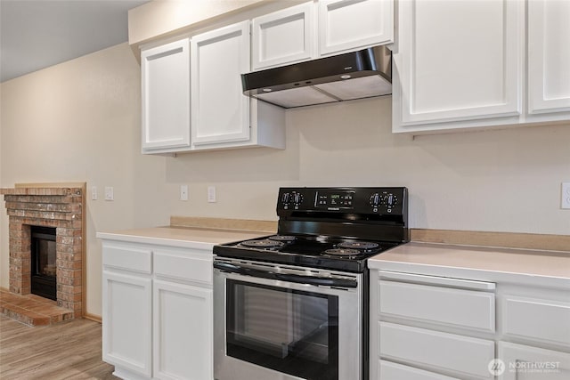 kitchen featuring under cabinet range hood, stainless steel electric stove, light countertops, a fireplace, and white cabinetry