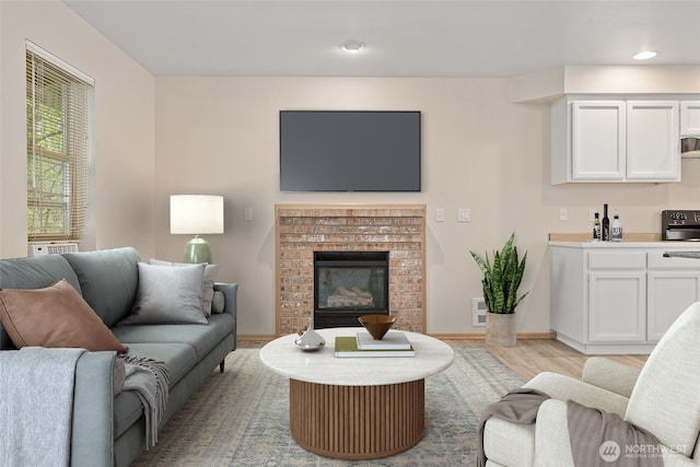 living room with a brick fireplace, recessed lighting, baseboards, and light wood finished floors