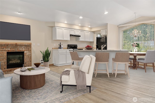 living area with lofted ceiling, recessed lighting, a fireplace, light wood-style floors, and a notable chandelier