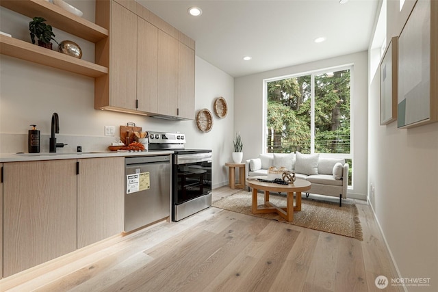 kitchen featuring stainless steel appliances, recessed lighting, light countertops, a sink, and light wood-type flooring