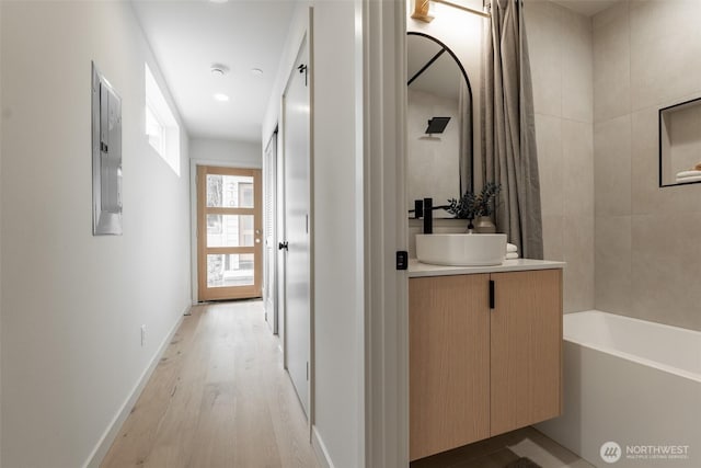 corridor with light wood finished floors, a sink, electric panel, and baseboards