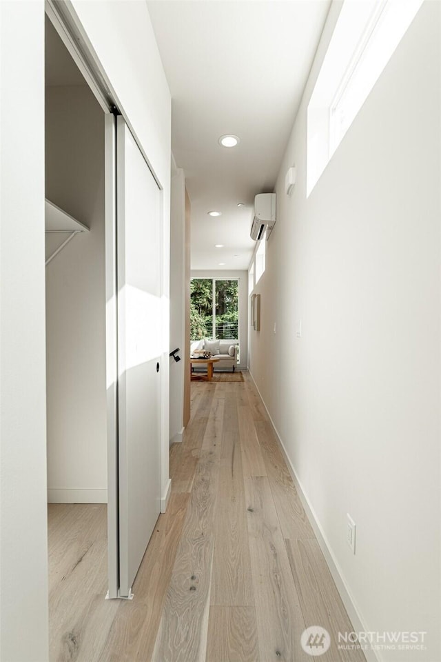 corridor with baseboards, an AC wall unit, light wood-style flooring, and recessed lighting