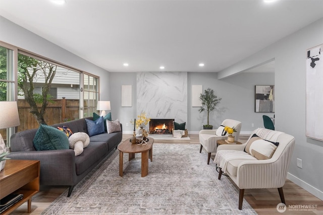 living area with recessed lighting, a premium fireplace, baseboards, and wood finished floors