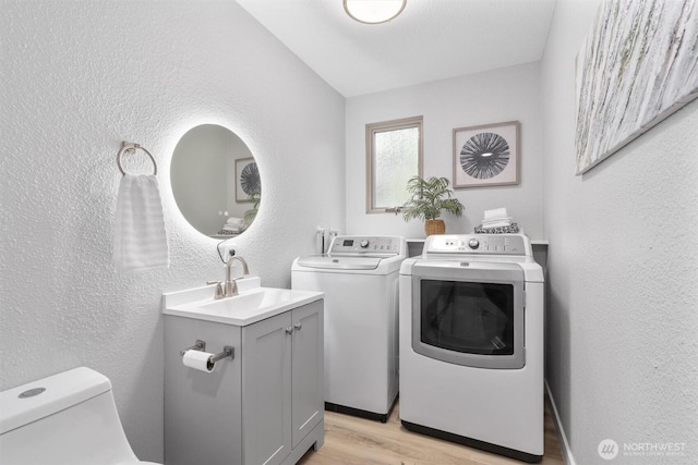 clothes washing area featuring light wood finished floors, laundry area, a textured wall, washer and dryer, and a sink