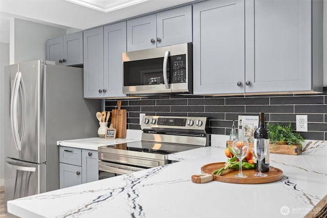 kitchen with decorative backsplash, gray cabinetry, light stone countertops, and stainless steel appliances