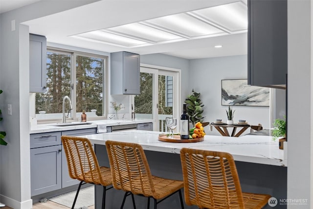 kitchen featuring gray cabinetry, a breakfast bar, light stone counters, light wood-style floors, and a sink