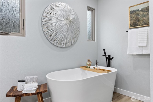 full bathroom featuring a soaking tub, baseboards, and wood finished floors