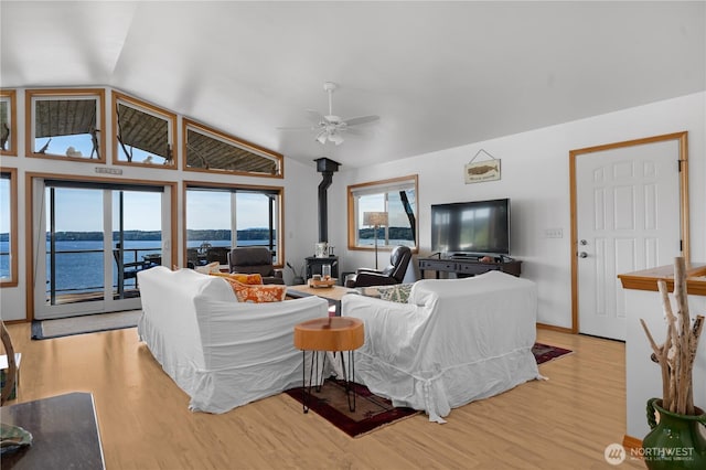 living room with vaulted ceiling, light wood-type flooring, a wood stove, and a ceiling fan