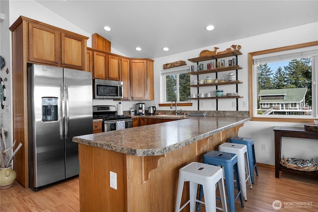 kitchen featuring brown cabinets, a peninsula, vaulted ceiling, stainless steel appliances, and open shelves