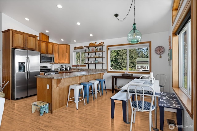 kitchen featuring appliances with stainless steel finishes, vaulted ceiling, light wood-style floors, a kitchen bar, and open shelves