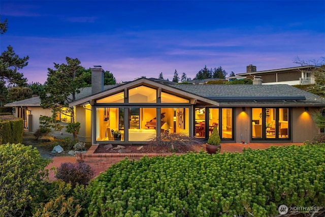 back of property at dusk featuring a chimney and a shingled roof