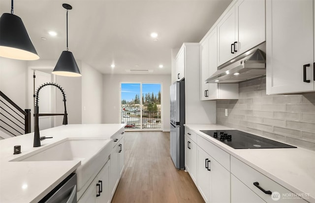 kitchen featuring light wood-style flooring, under cabinet range hood, stainless steel appliances, light countertops, and tasteful backsplash