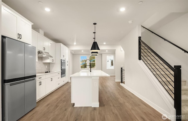 kitchen with light wood finished floors, white cabinets, appliances with stainless steel finishes, under cabinet range hood, and a sink