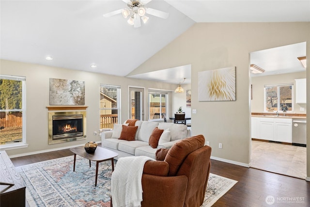 living room featuring high vaulted ceiling, recessed lighting, wood finished floors, baseboards, and a glass covered fireplace