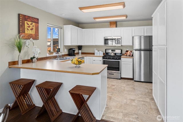 kitchen featuring white cabinets, a peninsula, stainless steel appliances, light countertops, and a sink