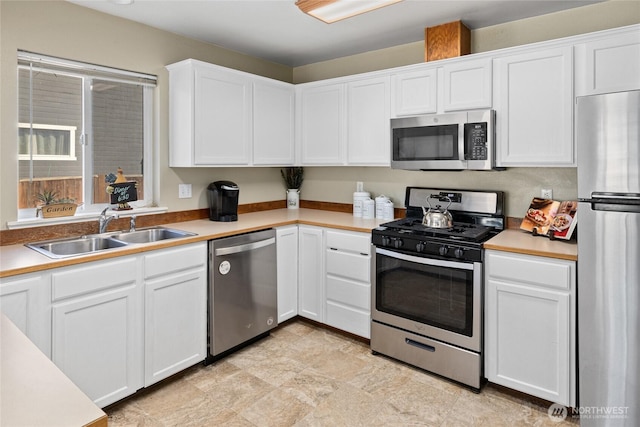 kitchen with appliances with stainless steel finishes, white cabinets, a sink, and light countertops