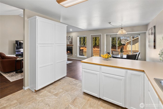 kitchen featuring a warm lit fireplace, white cabinetry, open floor plan, light countertops, and hanging light fixtures