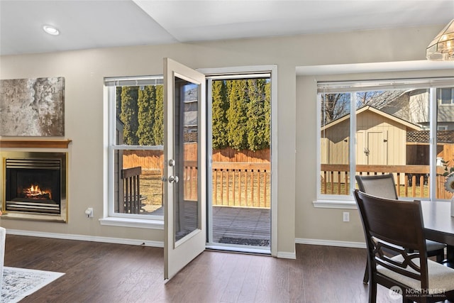 doorway to outside with a warm lit fireplace, wood finished floors, and baseboards