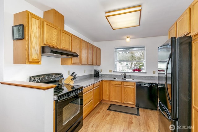 kitchen featuring light countertops, light wood-style floors, a sink, under cabinet range hood, and black appliances