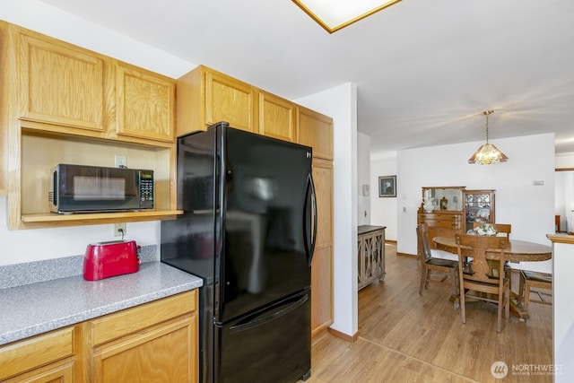 kitchen with light countertops, hanging light fixtures, light wood-style floors, black appliances, and baseboards