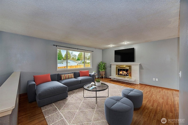 living room featuring a textured ceiling, a fireplace, baseboards, and wood finished floors