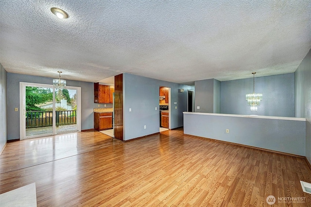 unfurnished living room featuring baseboards, light wood finished floors, visible vents, and an inviting chandelier