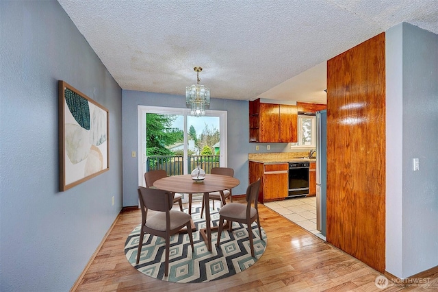 dining space with a chandelier, light wood-type flooring, a textured ceiling, and baseboards