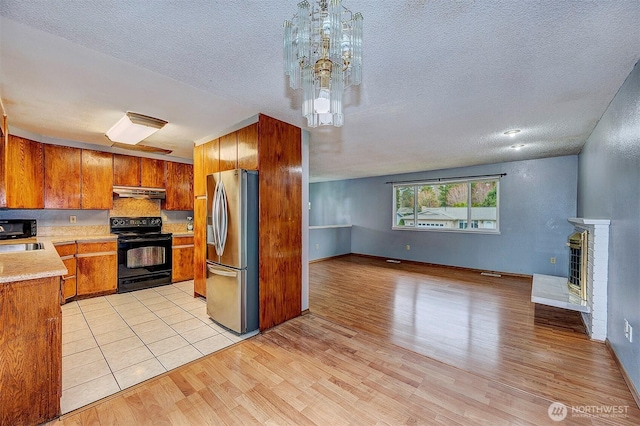 kitchen with black electric range, brown cabinets, stainless steel refrigerator with ice dispenser, open floor plan, and under cabinet range hood