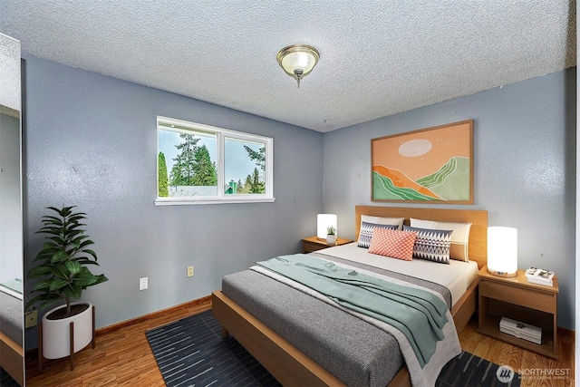 bedroom with a textured ceiling, baseboards, and wood finished floors