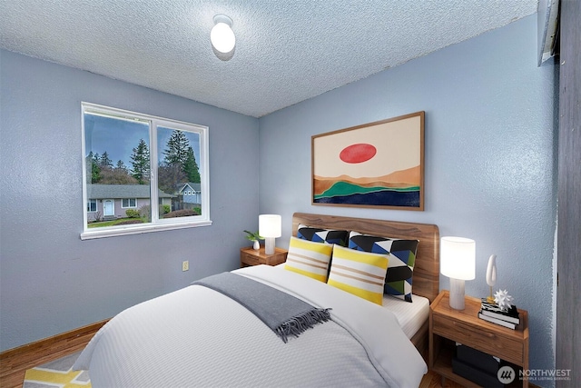 bedroom featuring a textured wall, baseboards, a textured ceiling, and wood finished floors