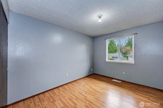 unfurnished room featuring visible vents, a textured wall, light wood-style flooring, a textured ceiling, and baseboards