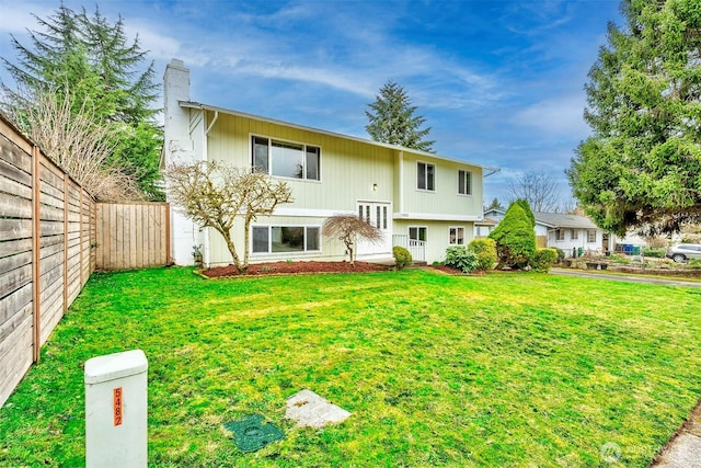 back of house with a chimney, fence, and a yard