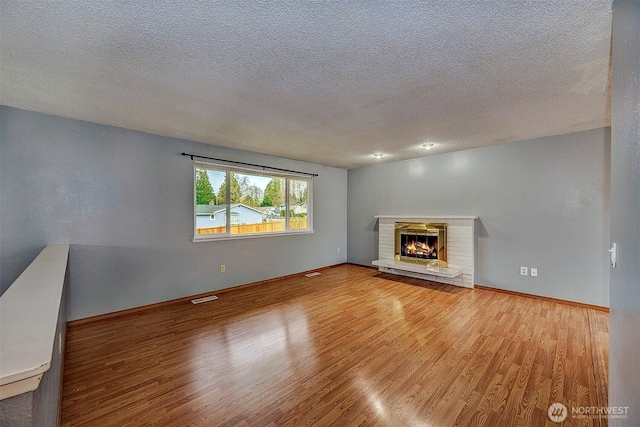 unfurnished living room featuring baseboards, visible vents, light wood-style floors, a textured ceiling, and a brick fireplace