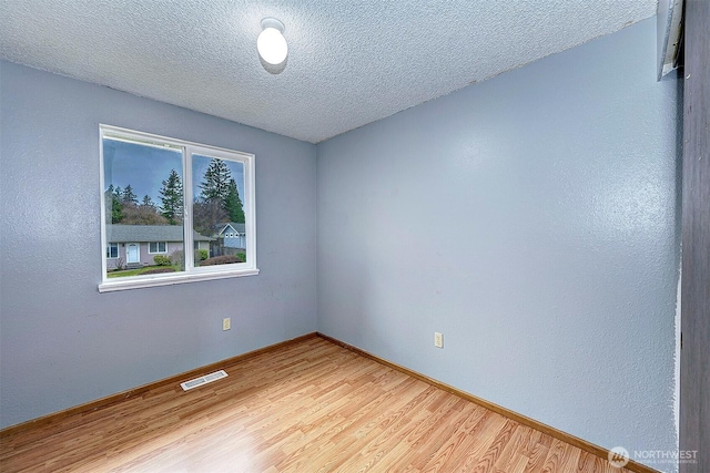 empty room with baseboards, visible vents, light wood-style flooring, and a textured ceiling