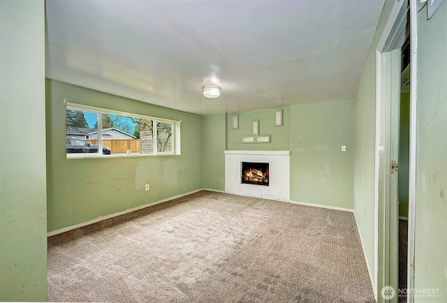 unfurnished living room featuring carpet floors, a warm lit fireplace, and baseboards